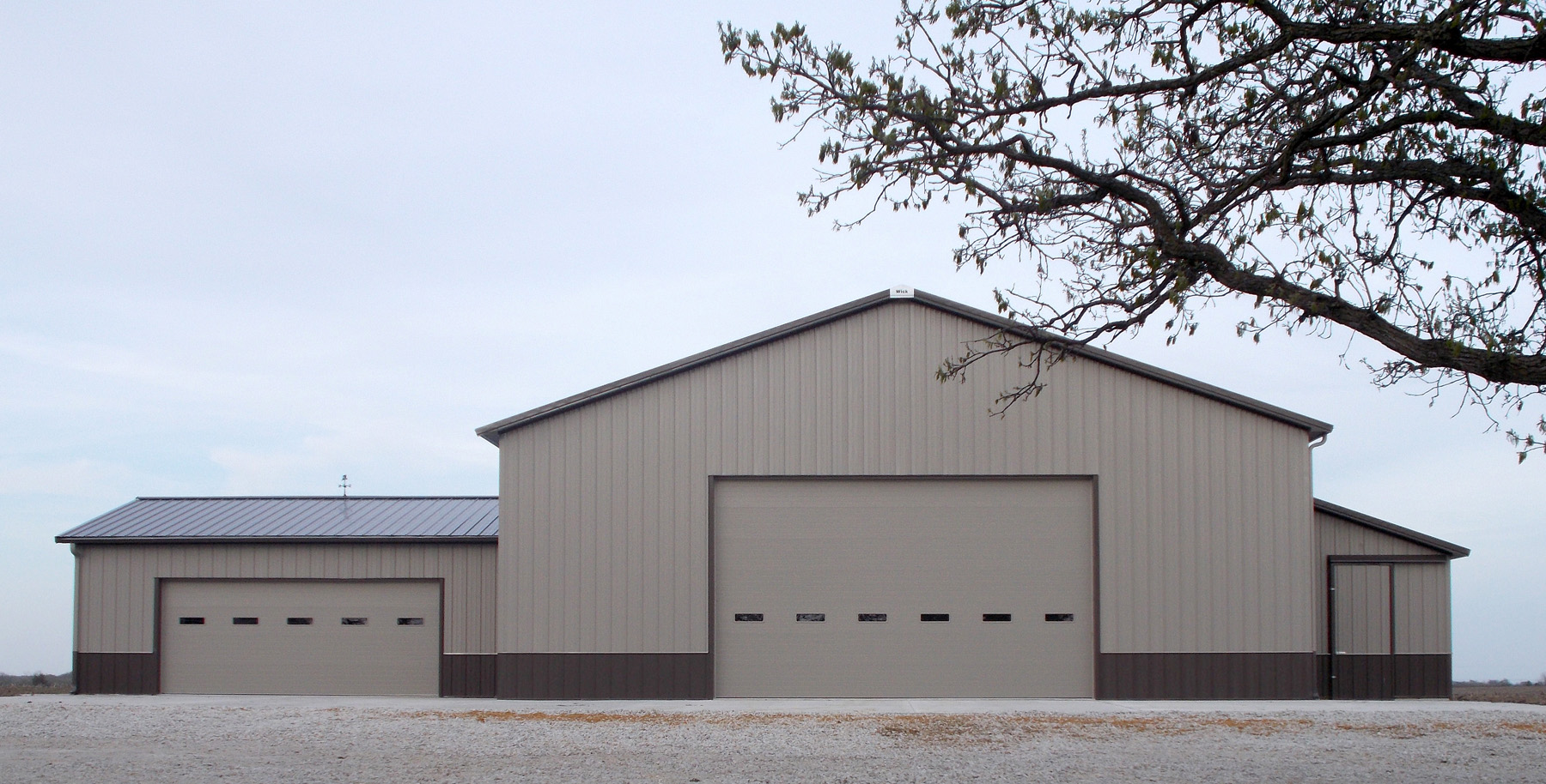 beige and brown post frame suburban building featuring two large garage doors