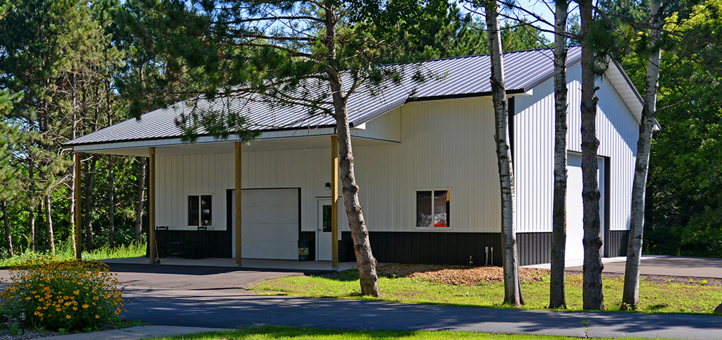 black and white post frame suburban building with large front awning and front and side garage doors