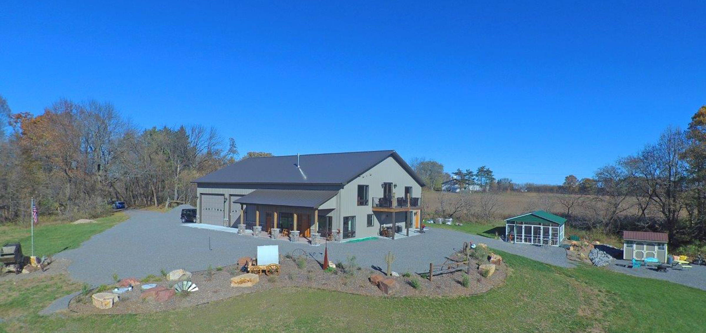 Post frame residential building perched on a hill featuring old West landscaping, two garages and an overhang roof and porch